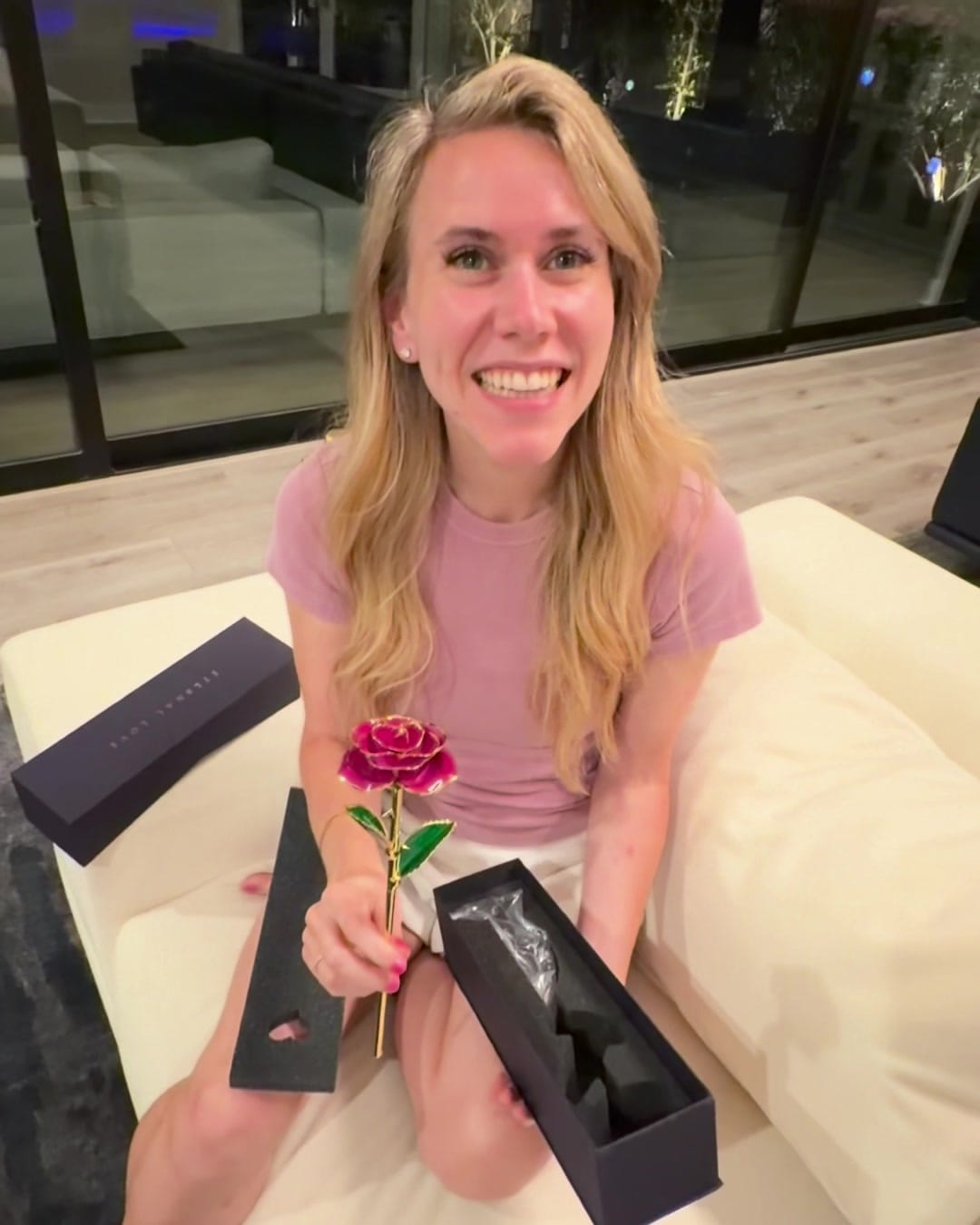 She holds the gold rose and smiles, the open box in her lap